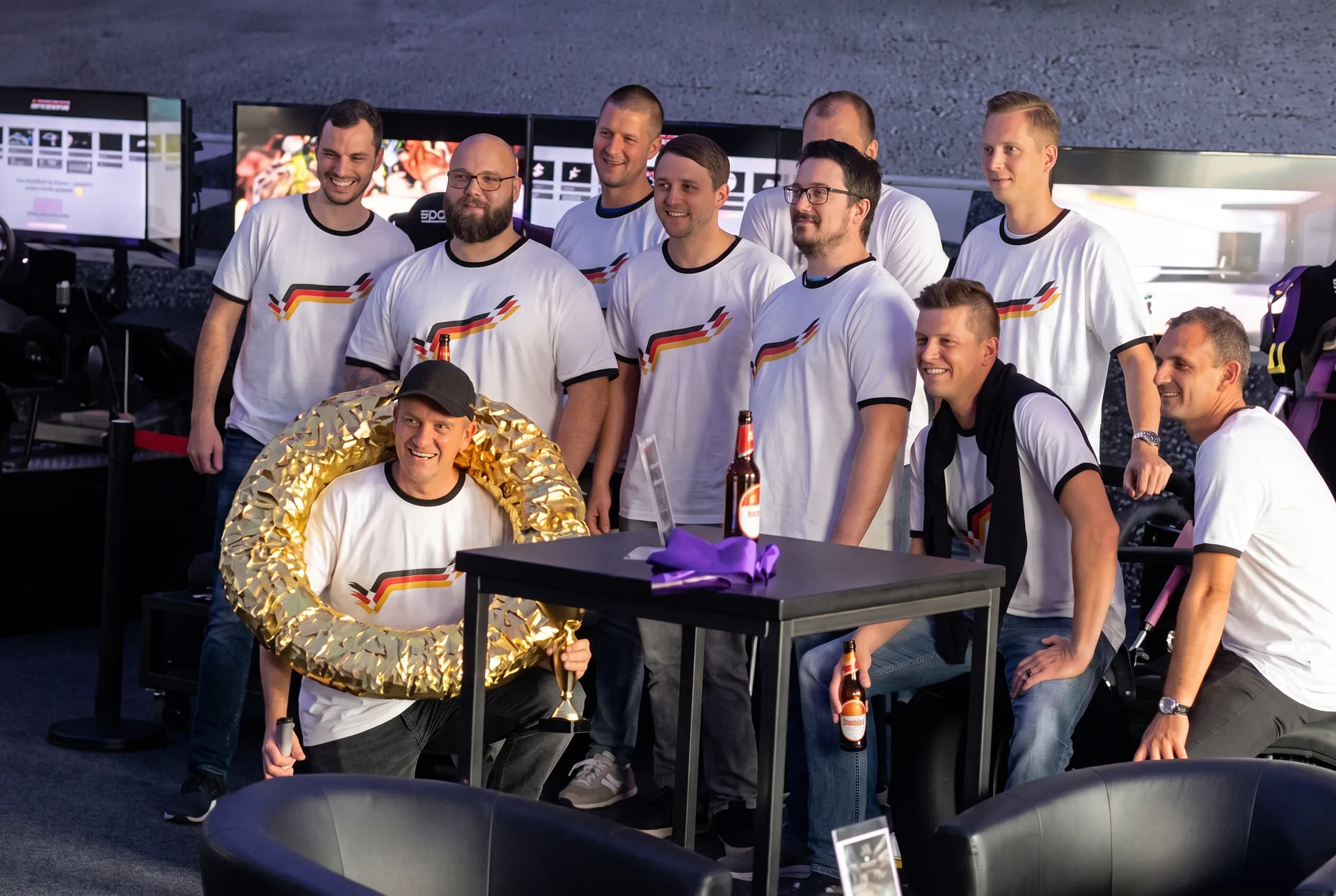 Junggesellenabschied in der Arena: Gruppe in weißen Shirts mit goldenem Siegerkranz vor den Simulatoren (Mit KI bearbeitet)